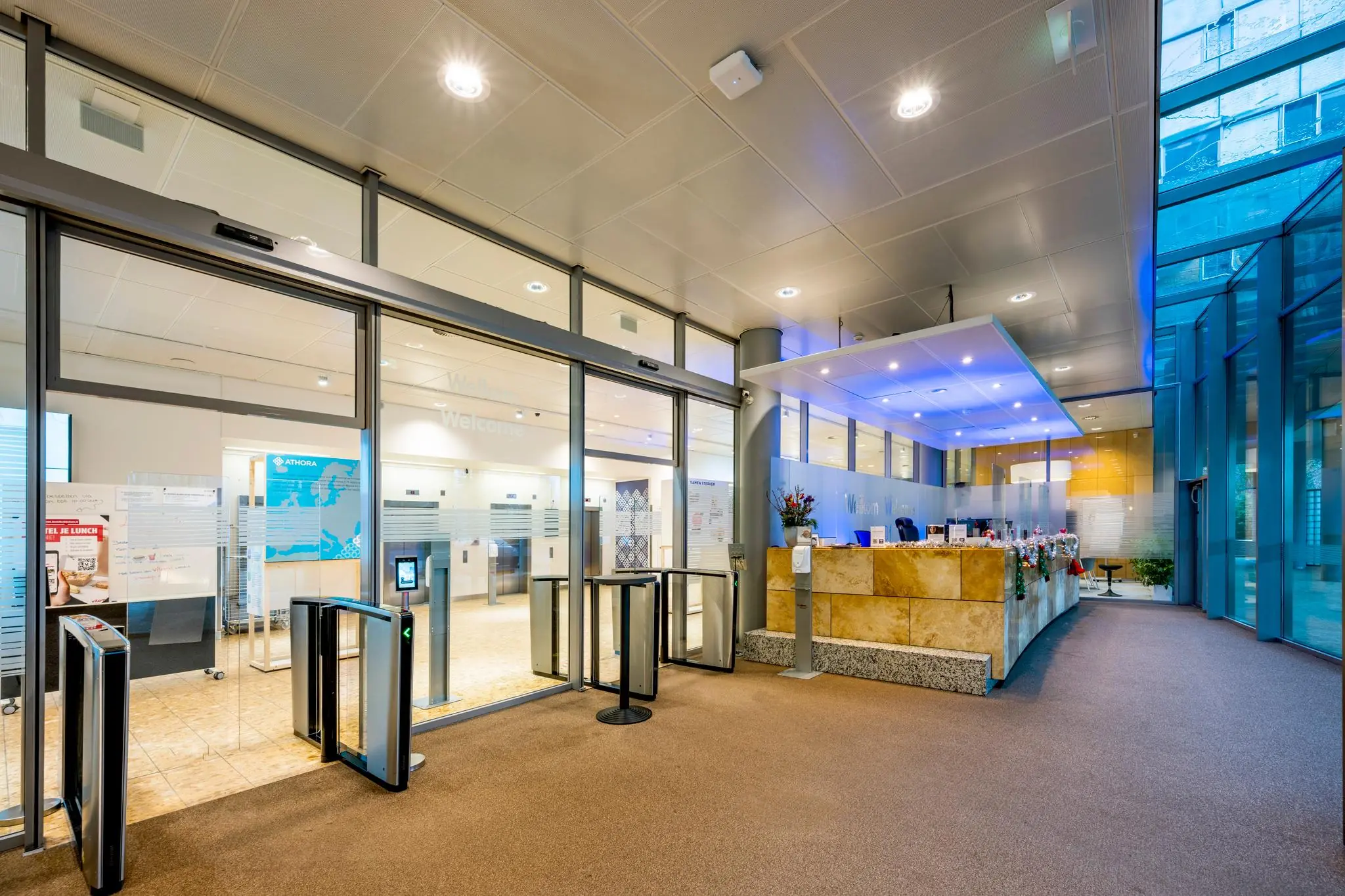 Moderne entreehal met receptiebalie en toegangspoortjes in een kantoorpand aan de Burgemeester Rijnderslaan.